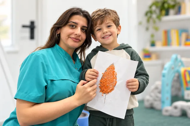 An educator in turquoise and a child holding an autumn craft.